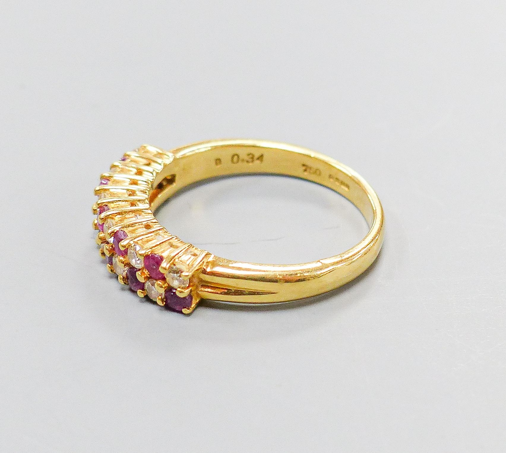 A modern 18ct gold, ruby and diamond set two row half hoop ring, size O, gross 5.3 grams.